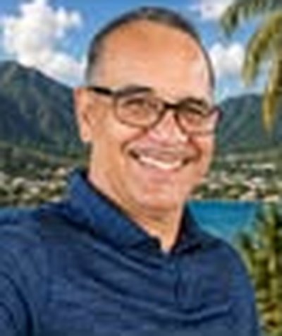 Portrait of Theodore (Ted) Leiato smiling in a blue shirt and glasses, with mountains and a bay behind him.